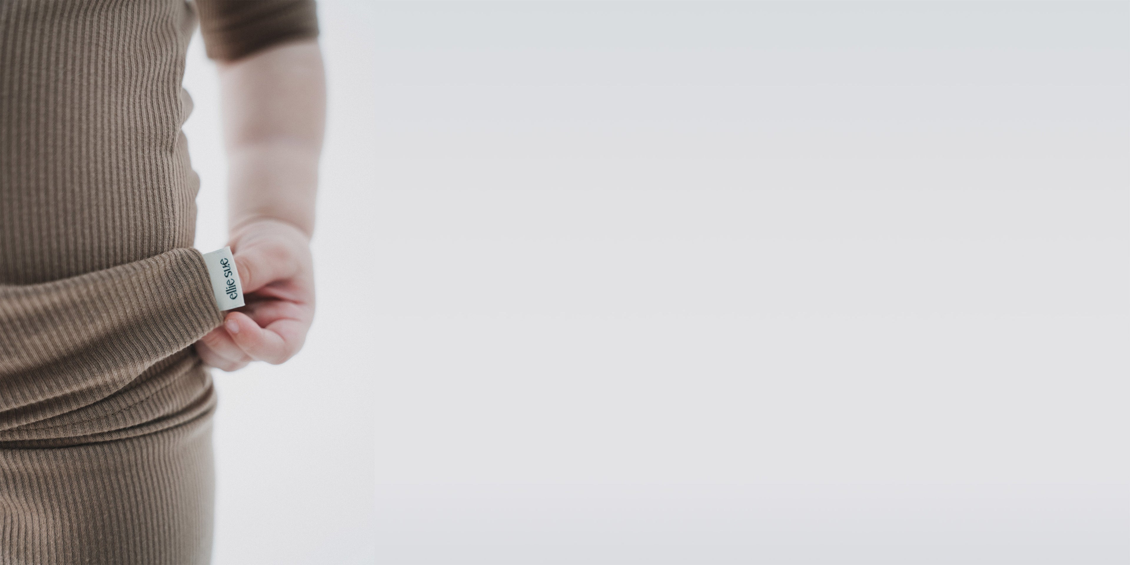 Toddler wearing a brown ribbed pajamas with a visible Ellie Sue brand label on a light gray background